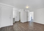 Thumbnail 6 of 56 - A room with white walls and wooden flooring with a door on the left.