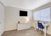 Thumbnail 29 of 56 - A room with a desk, chair, and a television mounted on the wall.