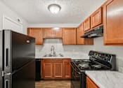 Thumbnail 11 of 15 - A black refrigerator is on the left in a kitchen with wooden cabinets.