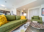 Thumbnail 5 of 15 - A living room with a green couch and a patterned rug.
