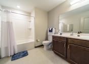 Thumbnail 15 of 15 - A bathroom with a white tub, a white toilet, a sink, and a blue rug.