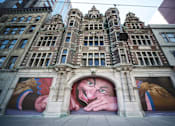 Thumbnail 1 of 15 - A mural of a man's face is painted on the side of a building.
