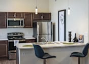 Thumbnail 9 of 15 - A kitchen with a white counter top and a black chair.