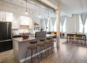 Thumbnail 11 of 19 - A kitchen with a black refrigerator and wooden floors.