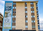 Thumbnail 1 of 10 - A tall building with a blue and beige facade and a sign that says Flats.