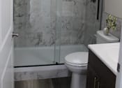 Thumbnail 16 of 18 - A white toilet sits in a marble bathroom next to a walk-in shower.