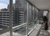 Thumbnail 15 of 18 - A balcony with glass doors overlooks a parking garage and buildings.