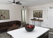 Thumbnail 11 of 18 - A living room with a brown couch, a white table, and a ceiling fan.