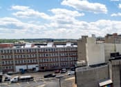 Thumbnail 4 of 10 - A cityscape with a large building in the foreground and a cloudy sky above.