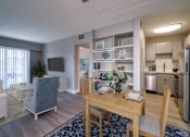 Thumbnail 6 of 10 - A dining room with a table set for two and a kitchen area in the background.