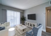 Thumbnail 9 of 10 - A living room with a white couch, a blue chair, and a television mounted on the wall.