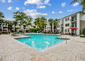 Thumbnail 12 of 18 - A swimming pool surrounded by a stone patio and palm trees.