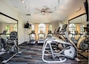 Thumbnail 16 of 18 - A gym with treadmills, elliptical machines, and a fan.