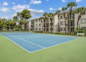 Thumbnail 13 of 18 - A tennis court is surrounded by palm trees and apartment buildings.
