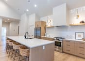 Thumbnail 6 of 82 - A modern kitchen with a long white island and stainless steel appliances.
