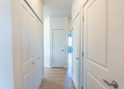 Thumbnail 61 of 82 - A long hallway with white doors and a wooden floor.