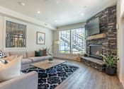 Thumbnail 25 of 36 - A modern living room with a grey couch, a fireplace, and a TV mounted on a stone wall at Forestplace Apartment Homes, Forest Grove
