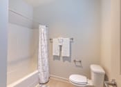 Thumbnail 35 of 36 - A white toilet sits next to a white shower curtain in a bathroom at Forestplace Apartment Homes, Forest Grove, OR