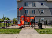 Thumbnail 17 of 25 - A playground with a red slide in front of a grey building at Northplace Apartment Homes, Salem, 97305
