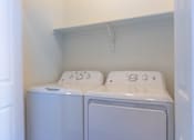 Thumbnail 19 of 72 - Two white front loading washing machines in a small laundry room at Riverplace Apartment Homes, Independence