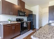 Thumbnail 38 of 72 - A kitchen with dark wood cabinets and black appliances at Riverplace Apartment Homes, Independence