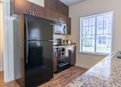 Thumbnail 40 of 72 - A black fridge in a kitchen with wooden cabinets and a window at Riverplace Apartment Homes, Oregon