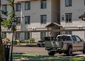 Thumbnail 58 of 72 - A large white building with a brown roof and a truck parked in front at Riverplace Apartment Homes, Independence, OR