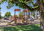 Thumbnail 61 of 72 - A playground with a slide and a tree in the foreground at Riverplace Apartment Homes, Oregon, 97351