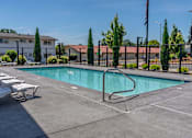 Thumbnail 4 of 22 - A pool surrounded by a fence and trees with chairs around it at St Helens Place Apartment Homes, Oregon