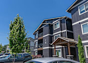 Thumbnail 8 of 22 - A grey building with a tree in front of it. at St Helens Place Apartment Homes, St Helens, OR