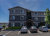 Thumbnail 9 of 22 - A grey apartment building with a parking lot in front at St Helens Place Apartment Homes, Oregon, 97051