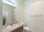 Thumbnail 22 of 46 - A bathroom with a sink, toilet, mirror, and a plant at Stoneplace Apartment Homes, Molalla, Oregon