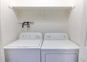 Thumbnail 23 of 46 - Two white washing machines in a small laundry room at Stoneplace Apartment Homes, Oregon, 97038