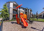 Thumbnail 9 of 12 - A playground with a slide and a climbing frame in front of a residential building at Timberridge Place Apartment Homes, Albany, OR