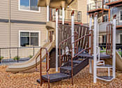 Thumbnail 9 of 49 - A playground with a slide and a climbing frame in front of apartment buildings at Woodburn Place Apartment Homes, Woodburn, 97071