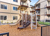 Thumbnail 10 of 49 - A playground with a slide and a climbing frame in front of apartment buildings at Woodburn Place Apartment Homes, Woodburn, Oregon