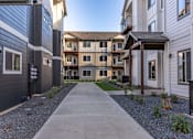 Thumbnail 14 of 49 - A concrete walkway leads to a building with a balcony at Woodburn Place Apartment Homes, Woodburn, 97071