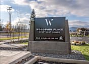 Thumbnail 17 of 49 - A sign for Woodburn Place Apartment Homes stands in front of a parking lot at Woodburn Place Apartment Homes, Oregon, 97071