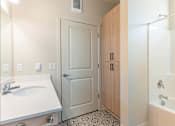 Thumbnail 44 of 49 - A bathroom with a sink, a door, and a bathtub at Woodburn Place Apartment Homes, Woodburn, Oregon