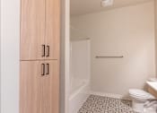 Thumbnail 47 of 49 - A bathroom with a toilet, sink, and wooden cabinet at Woodburn Place Apartment Homes, Oregon