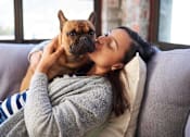 Thumbnail 3 of 3 - A woman is cuddling with a dog on a grey couch at The Hub Hermiston Apartments, Hermiston, Oregon