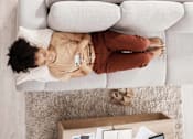 Thumbnail 2 of 3 - A person is lying on a grey couch with a remote control in hand at The Hub Hermiston Apartments, Hermiston, 97838