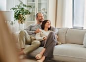 Thumbnail 1 of 3 - A man and woman are sitting on a couch, holding hands and smiling at each other at The Hub Hermiston Apartments, Hermiston