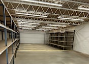 Thumbnail 5 of 5 - A large empty warehouse with metal shelving and a concrete floor.
