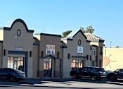 Thumbnail 1 of 5 - A row of stores with cars parked in front.