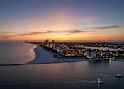 Thumbnail 11 of 13 - A beautiful sunset over a coastal city with boats in the water.