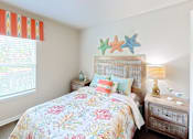 Thumbnail 6 of 13 - A bedroom with a floral bedspread and a wooden nightstand.