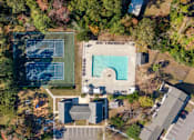 Thumbnail 15 of 16 - An aerial view of a tennis court and a swimming pool surrounded by trees and buildings.