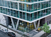 Thumbnail 1 of 16 - A modern building with glass windows and a tree in front.