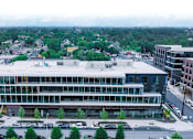 Thumbnail 2 of 16 - A large glass building with a parking lot in front.